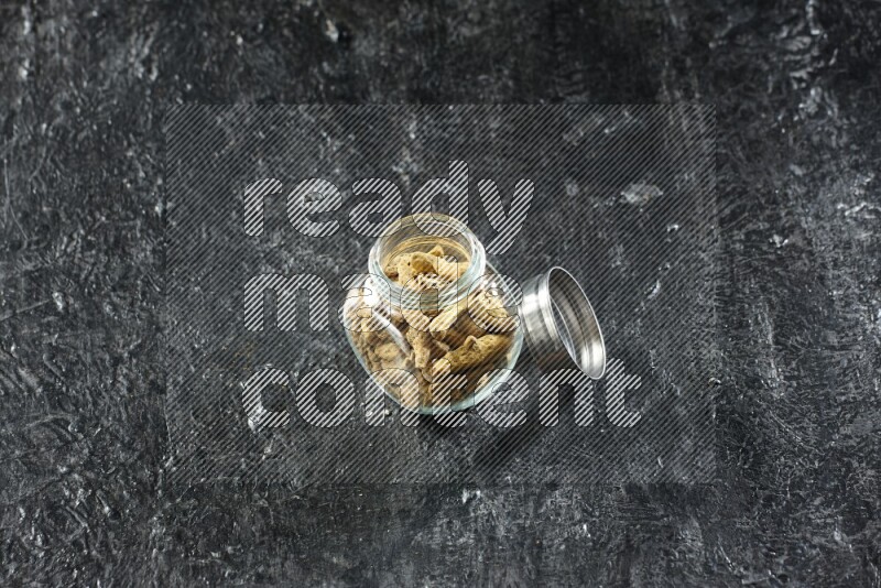 A glass spice jar full of dried turmeric whole fingers on a textured black flooring