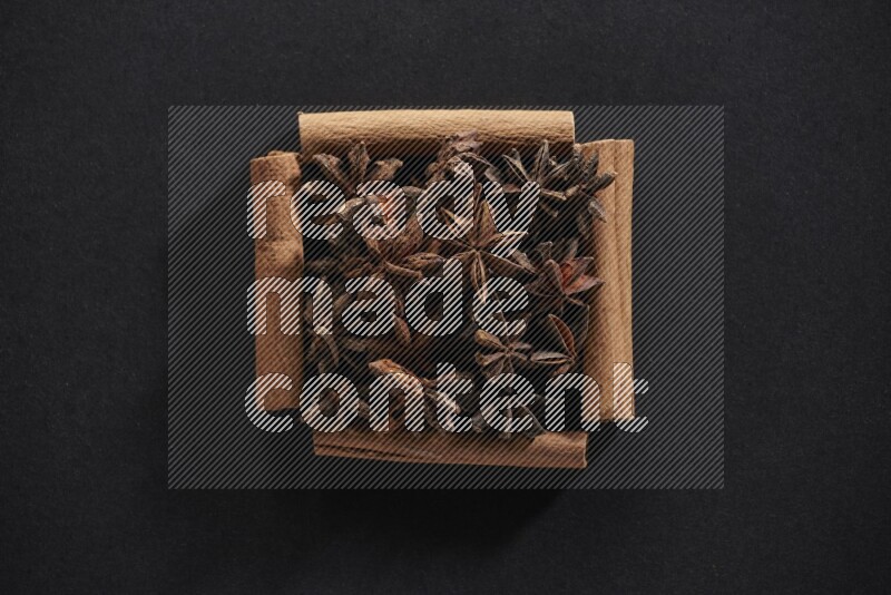 أربعة من أعواد القرفة مكونة شكل مربع بداخلها يانسون نجمي علي خلفية سوداء