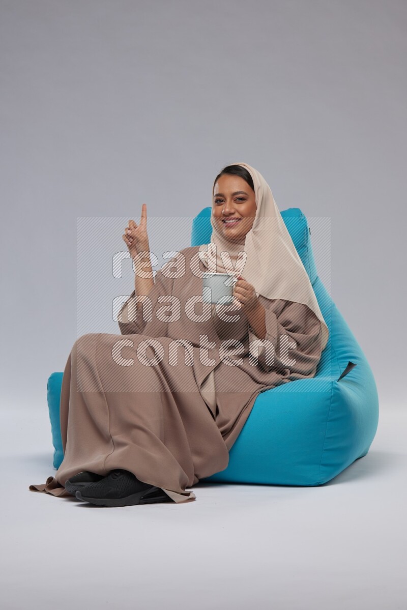 A Saudi woman sitting on a blue beanbag and drinking coffee