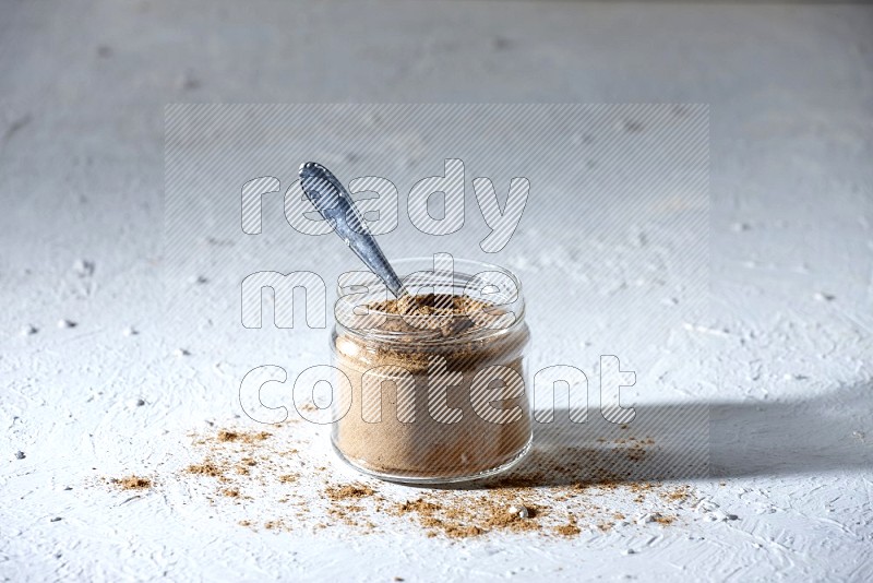 وعاء زجاجي وملعقة معدنية ممتلئة ببودرة بهار الفلفل الحلو على خلفية بيضاء