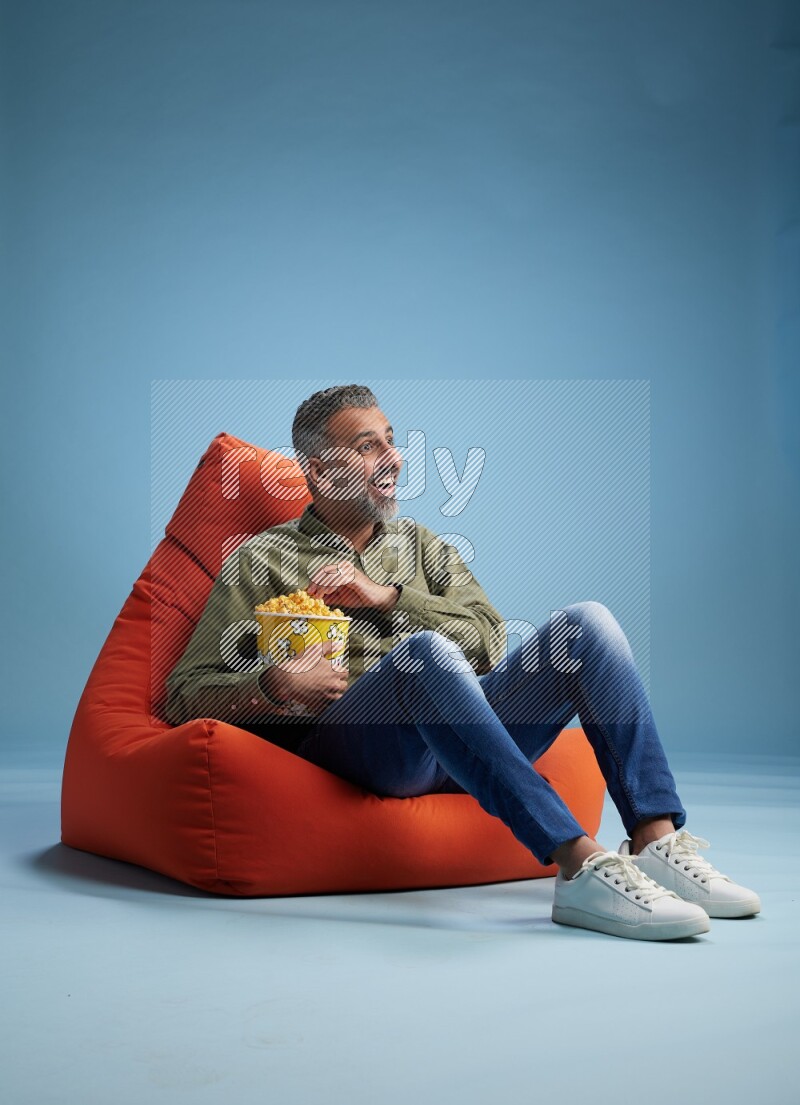 A man sitting on an orange beanbag and eating popcorn