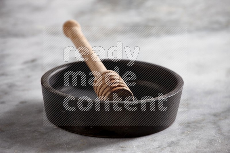 Black Pottery Oven Plate with wooden honey handle in it, on grey marble flooring, 15 degree angle