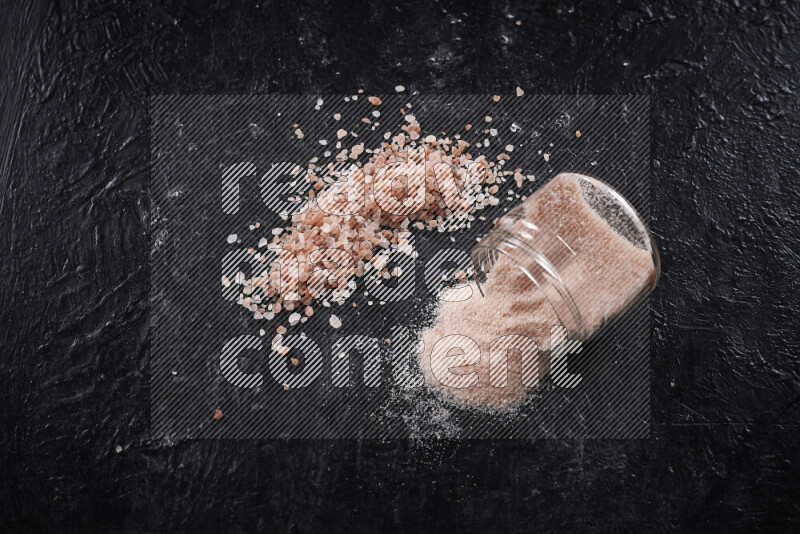 A glass jar full of fine himalayan salt with some himalayan crystals beside it on a black background