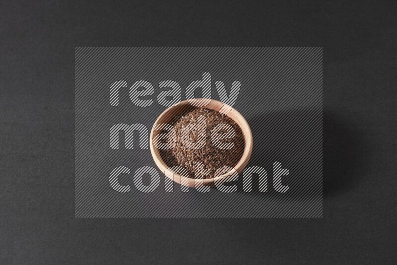 A wooden bowl full of flaxseeds on a black flooring