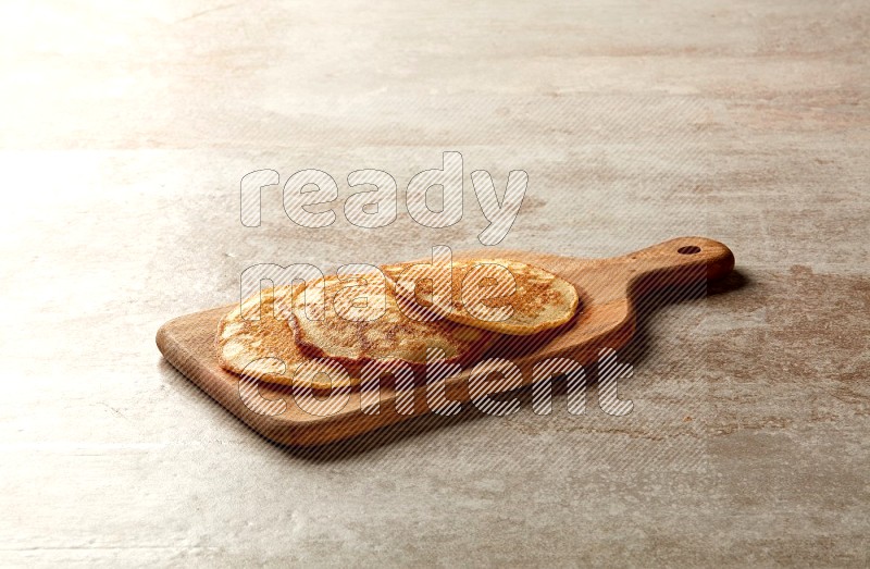 Three stacked plain pancakes on a wooden board on beige background