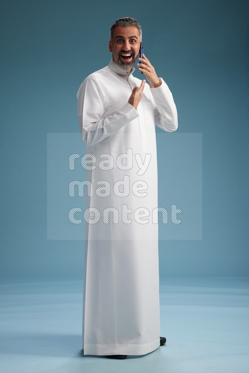 Saudi man wearing thob talking on the phone on blue background