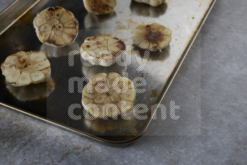 half's roasted garlic in a stainless tray on a grey textured countertop