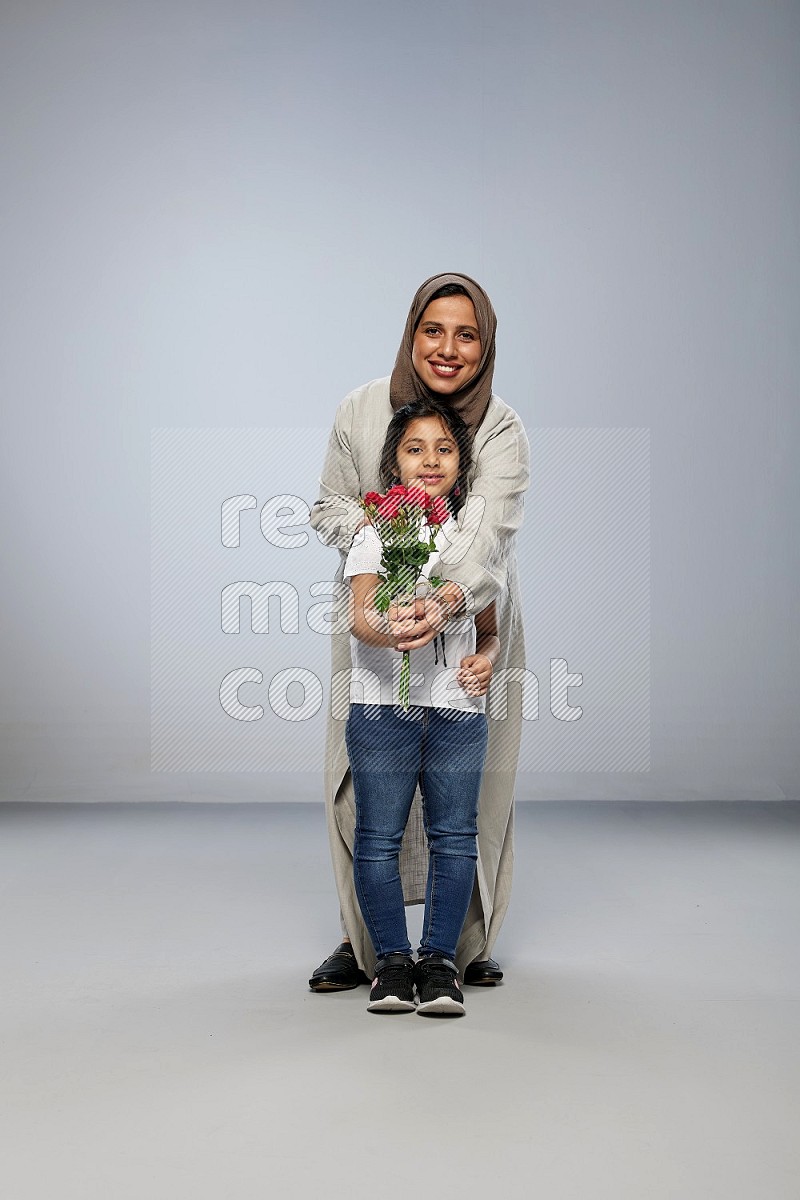 A girl standing giving flowers to her mother on gray background