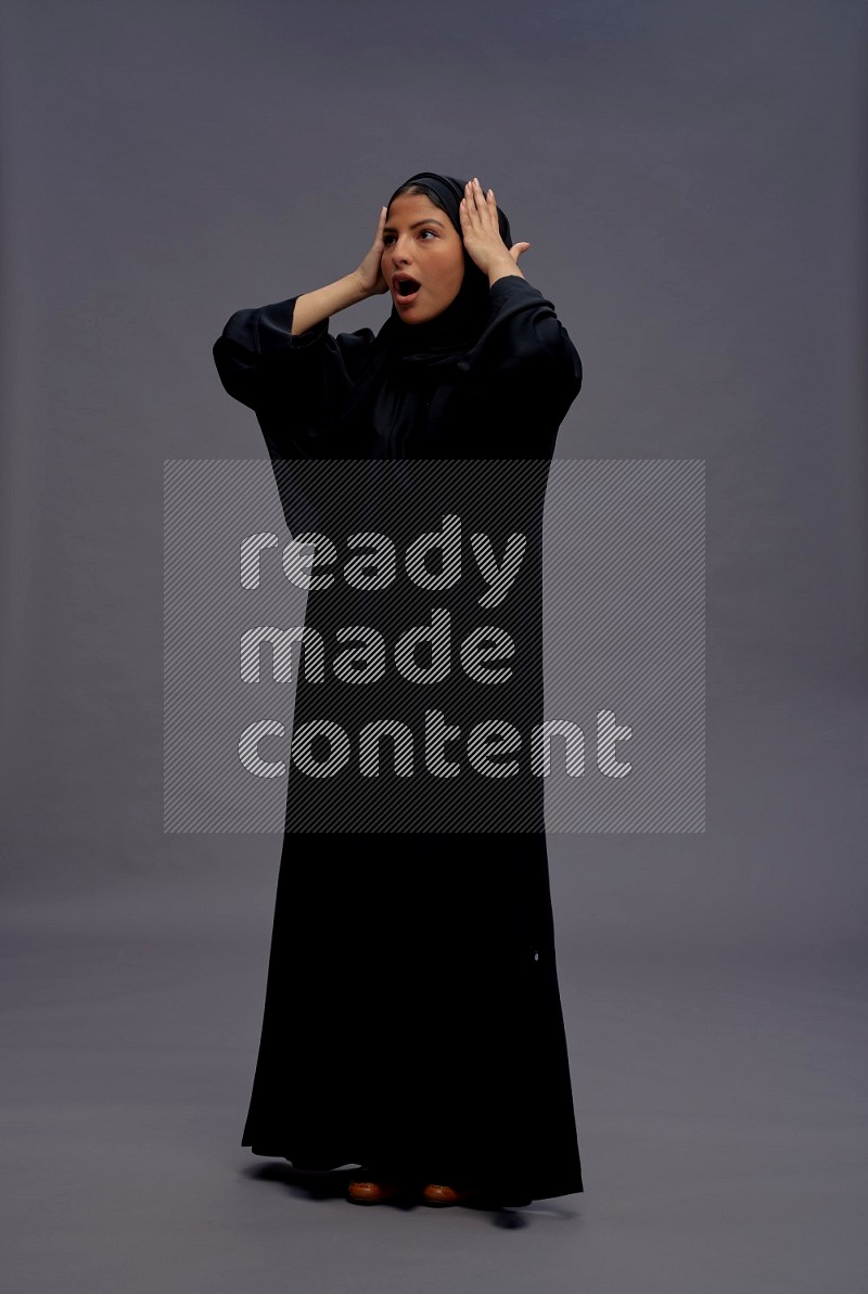 Saudi woman wearing Abaya standing hands behind head on gray background