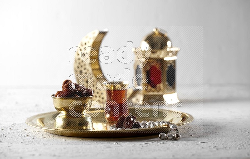 Dates in a metal bowl with tea and prayer beads on a tray beside lanterns in a light setup