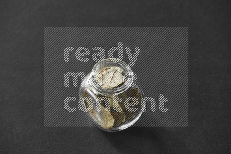 A glass spice jar full of bay laurel leaves on black flooring