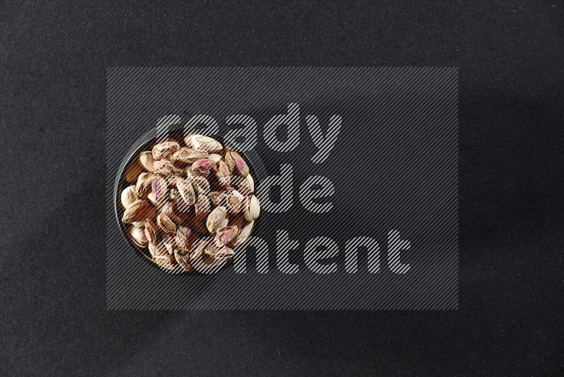 A black pottery bowl full of peeled pistachios on a black background in different angles