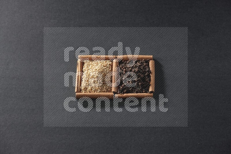 مربعان من أعواد القرفة ممتلئان ببذور السمسم والقرنفل علي خلفية سوداء