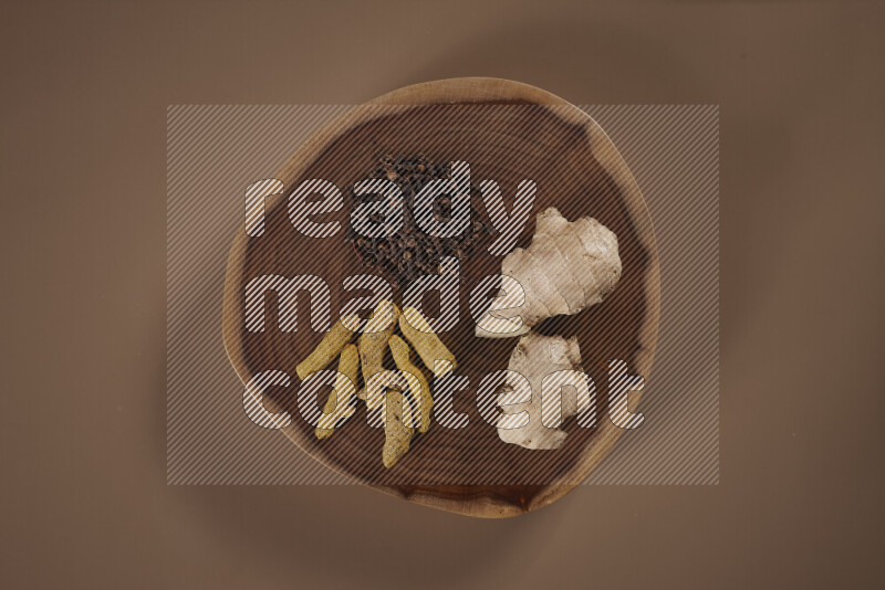 An assorted whole spices on a flat wooden tray including fresh and dried ginger, cinnamon sticks, cardamom, turmeric fingers, cloves, star anise on beige background