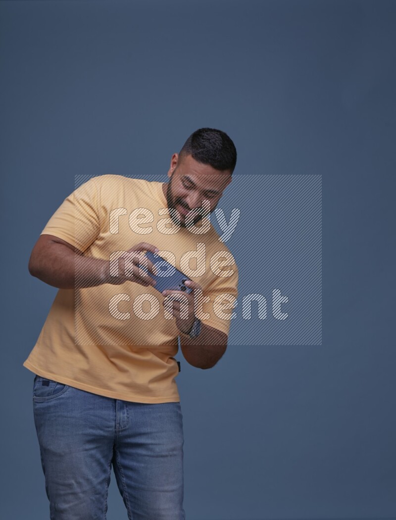 رجل يرتدي بنطال ازرق جينز وقميص اصفر بأكمام قصيره يلعب في جواله