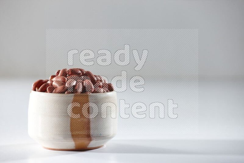 A beige ceramic bowl full of red skin peanuts on a white background in different angles