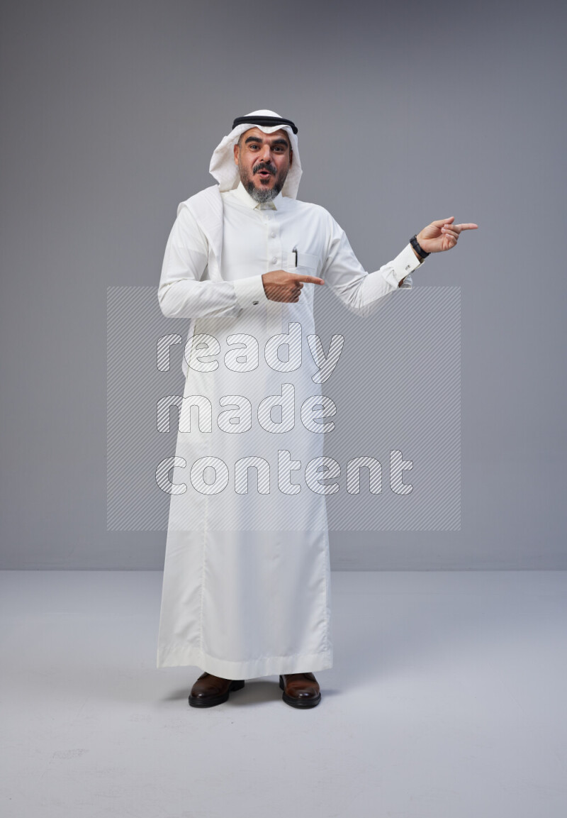 Saudi man Wearing Thob and white Shomag standing interacting with the camera on Gray background