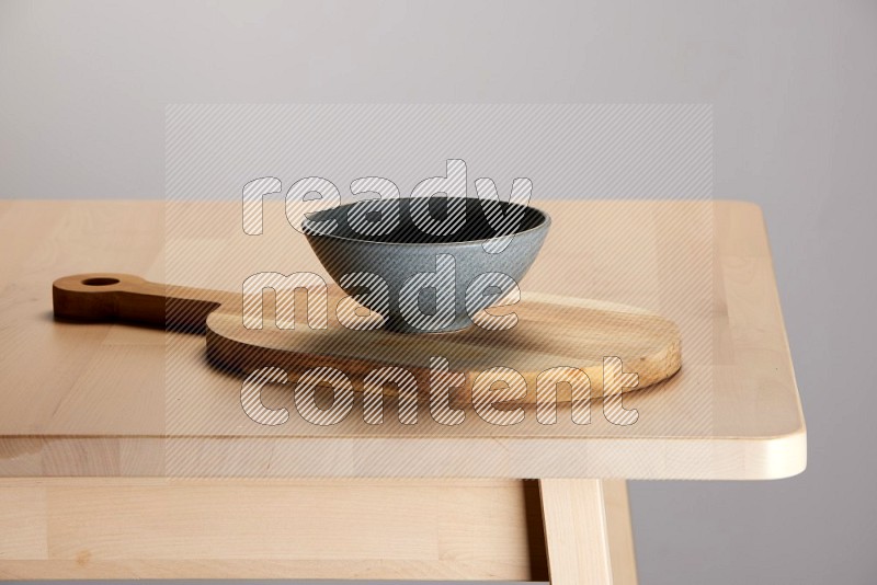 grey bowl placed on a  wooden oval cutting board on the edge of wooden table