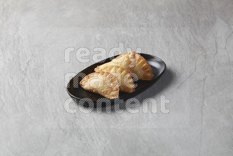Four fried sambosas in an oval shaped black plate on a gray background