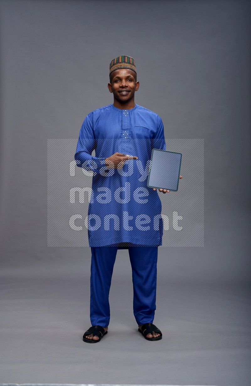 Man wearing Nigerian outfit standing showing tablet to camera on gray background