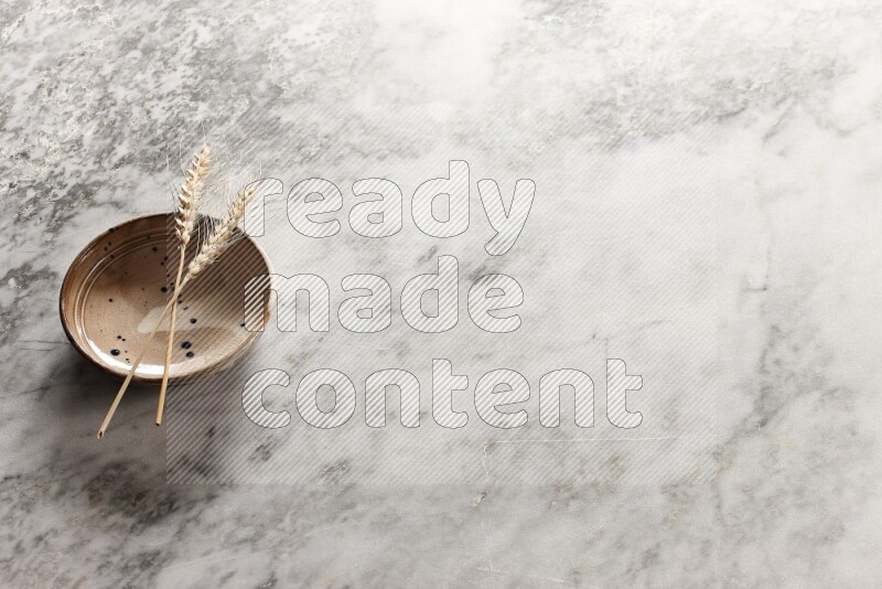Wheat stalks on multicolored pottery bowl on grey marble background