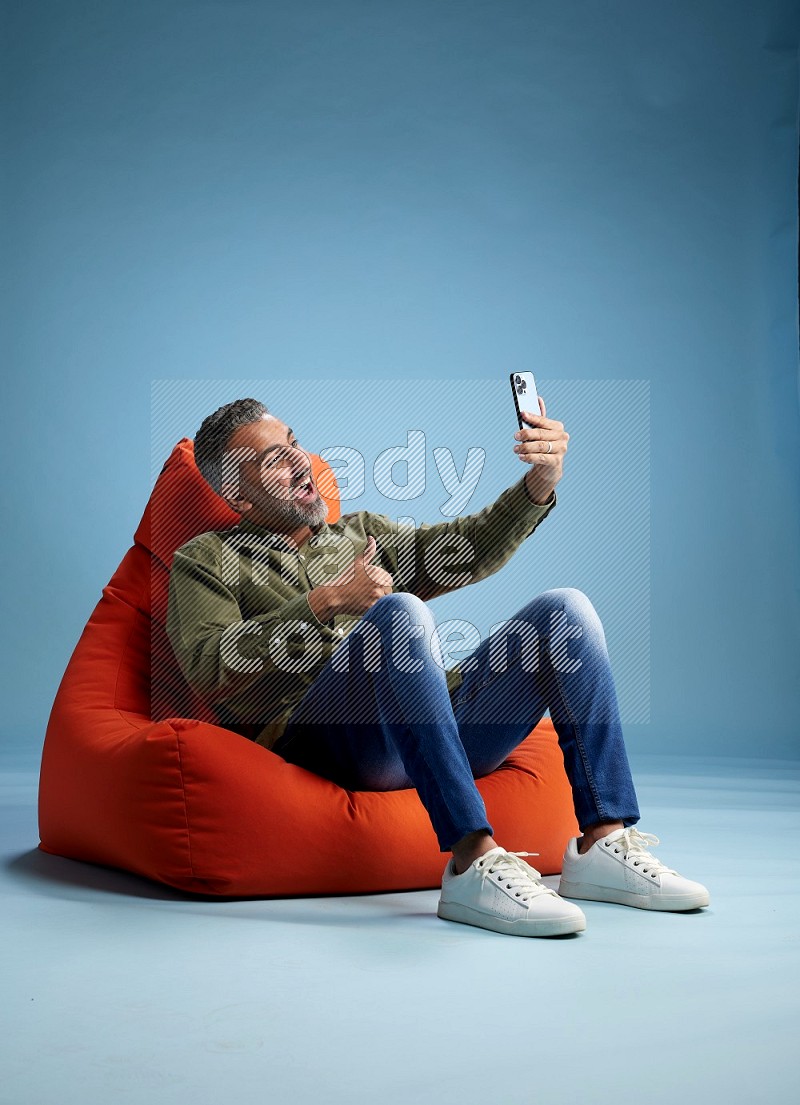 A man sitting on an orange beanbag and taking selfie