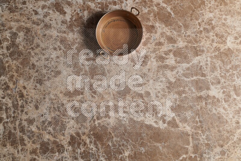 A small copper pan on beige marble background