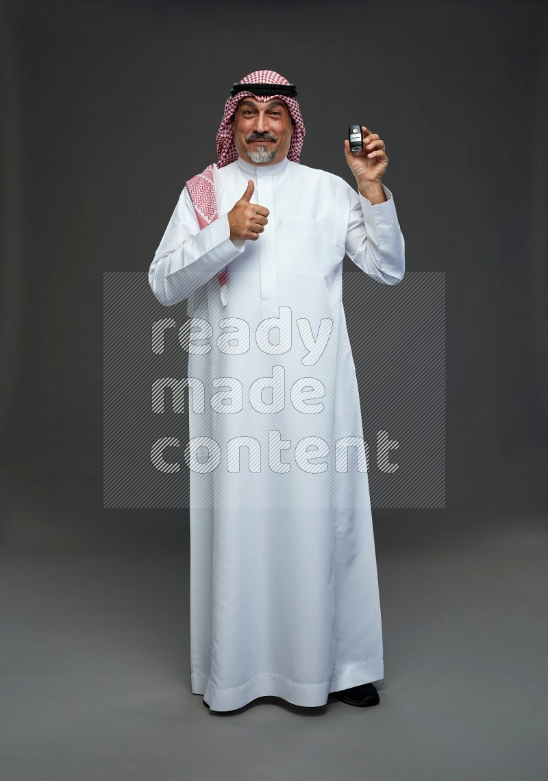 Saudi man with shomag Standing holding car key on gray background