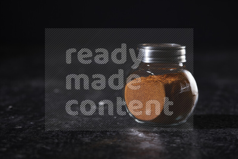 A glass jar full of ground paprika powder on black background