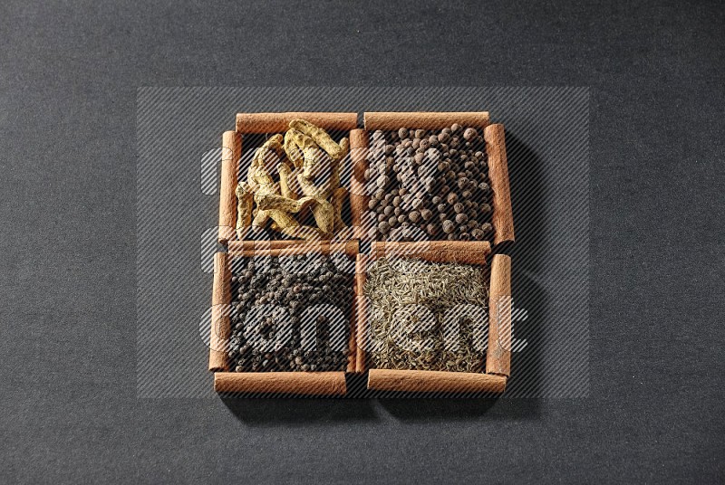 4 squares of cinnamon sticks full of black pepper, cumin, allspice and turmeric fingers on black flooring