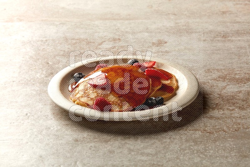 Three stacked mixed berries pancakes in a grey plate on beige background
