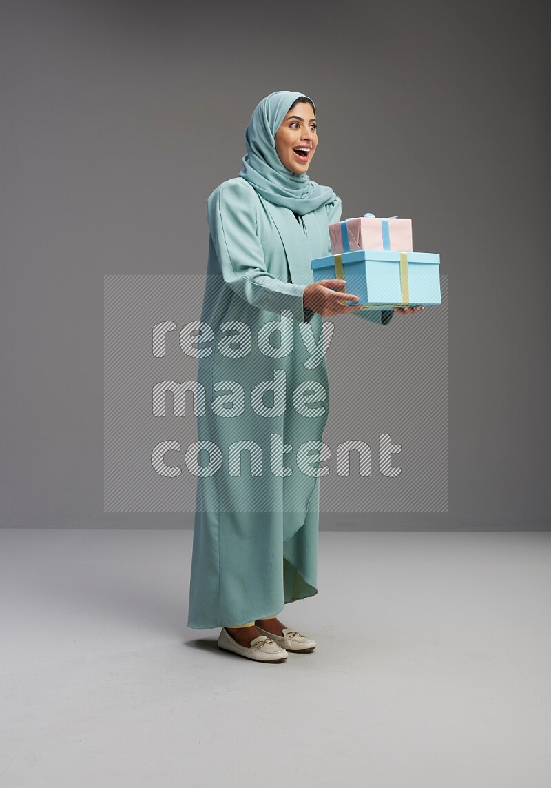 Saudi Woman wearing Abaya standing holding gift box on Gray background