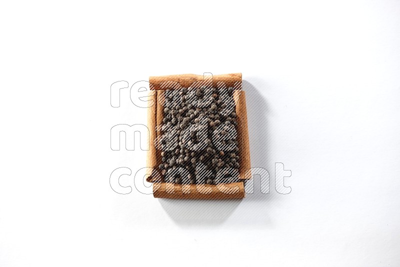 A single square of cinnamon sticks full of black pepper on white flooring