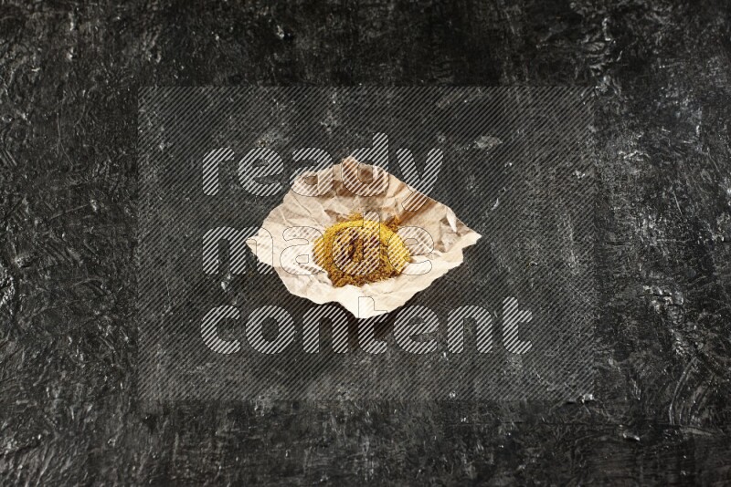 Turmeric powder in a crumpled piece of paper on textured black flooring