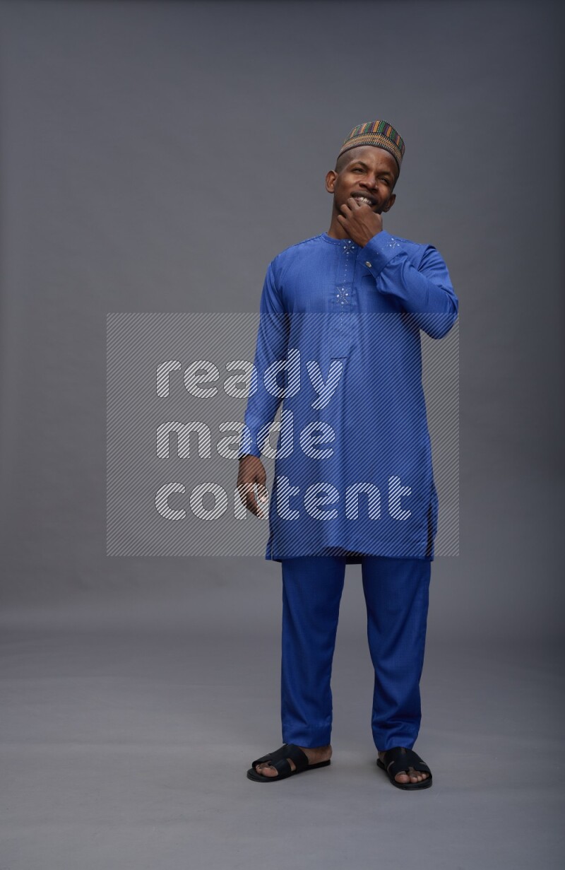 Man wearing Nigerian outfit standing interacting with the camera on gray background