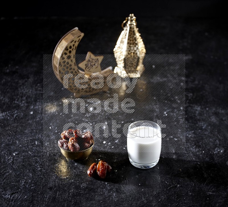 Dates in a metal bowl with milk beside golden lanterns in a dark setup
