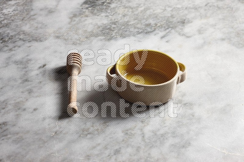 Multicolored Pottery bowl with wooden honey handle on the side with grey marble flooring, 45 degree angle