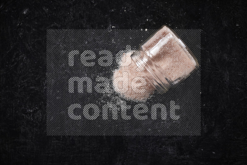 A glass jar full of fine himalayan salt on black background