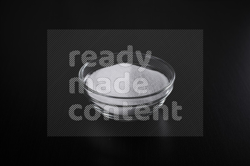 A glass bowl full of fine table salt on black background