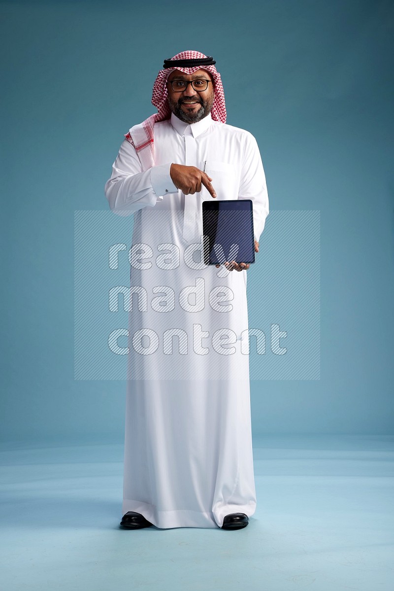 Saudi Man with shimag Standing holding a tablet on blue background