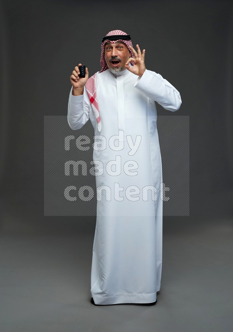 Saudi man with shomag Standing holding car key on gray background