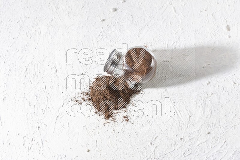 A flipped glass spice jar full of cloves powder and powder came out of it on textured white flooring