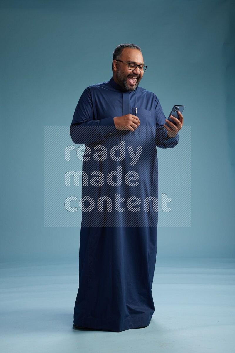 Saudi Man without shimag Standing texting on phone on blue background
