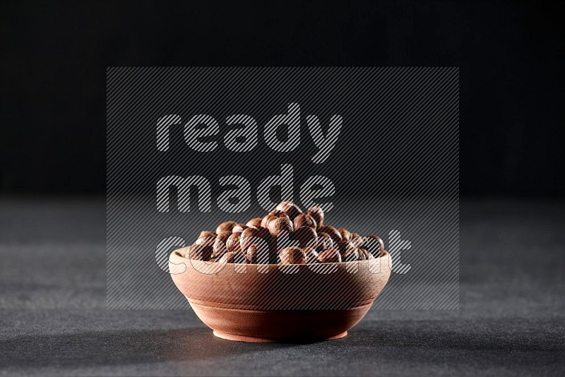 A wooden bowl full of peeled hazelnuts on a black background in different angles
