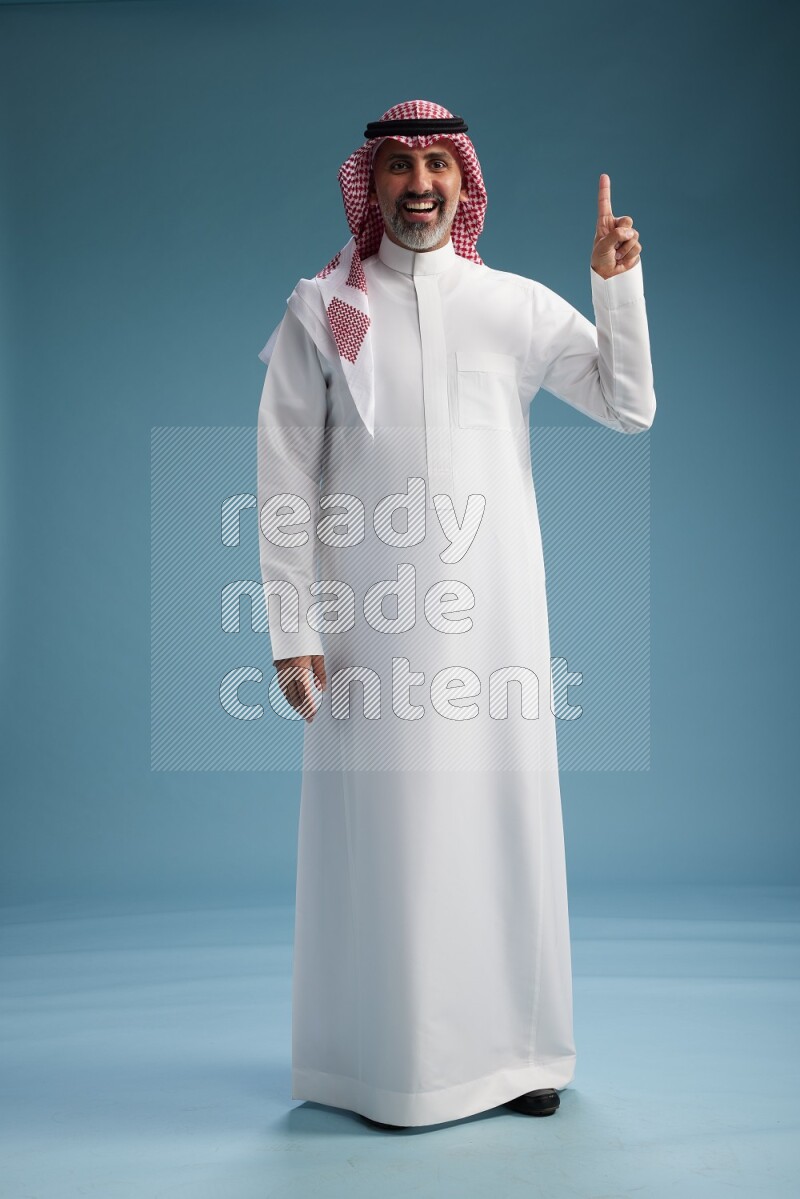 Saudi man wearing thob and shomagh posing to the camera on blue background