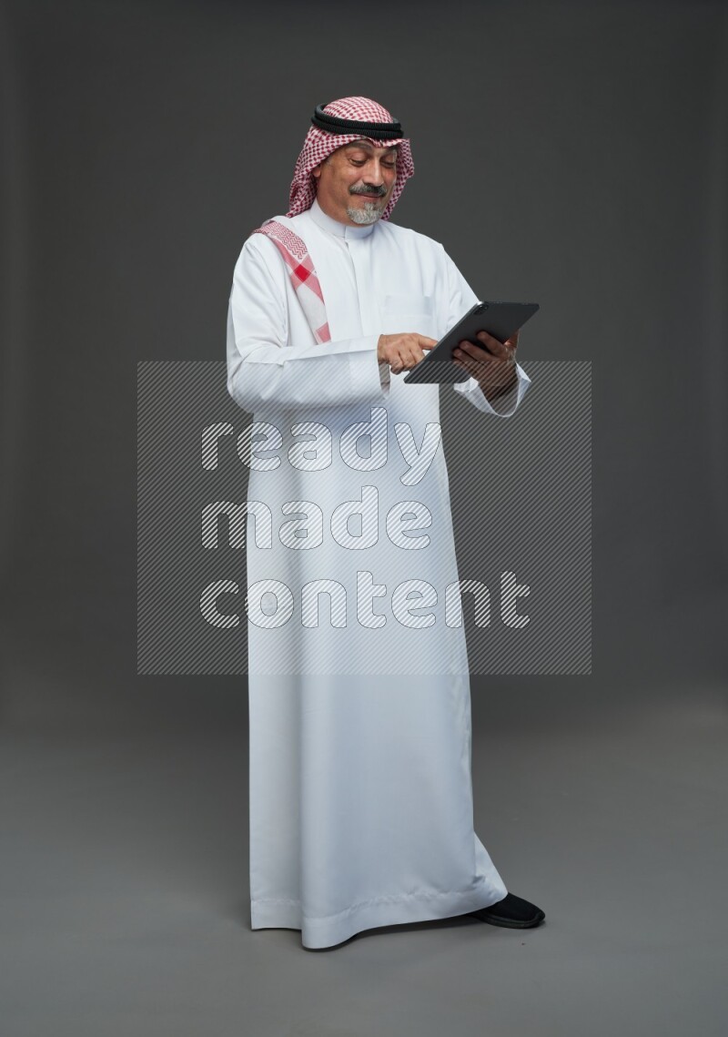 Saudi man with shomag Standing working on tablet on gray background