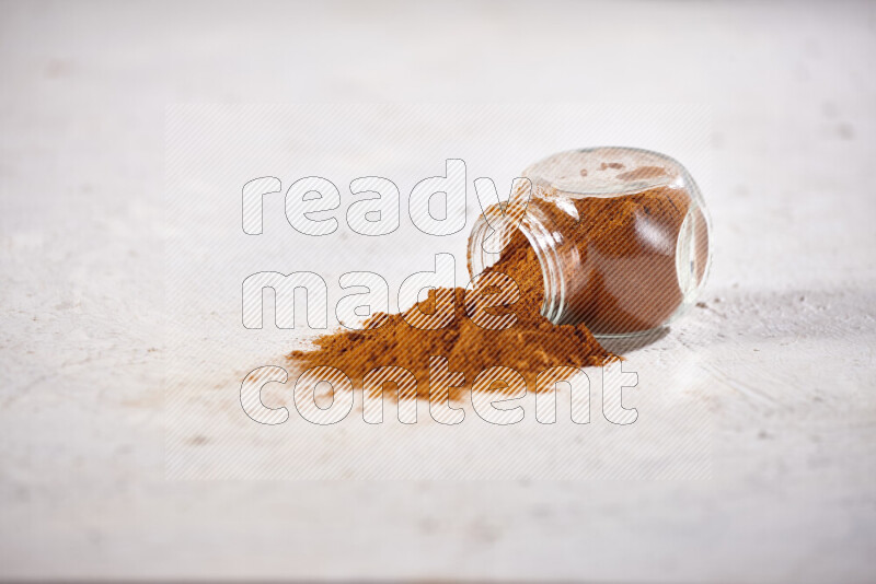 A glass jar full of ground paprika powder flipped with some spilling powder on white background