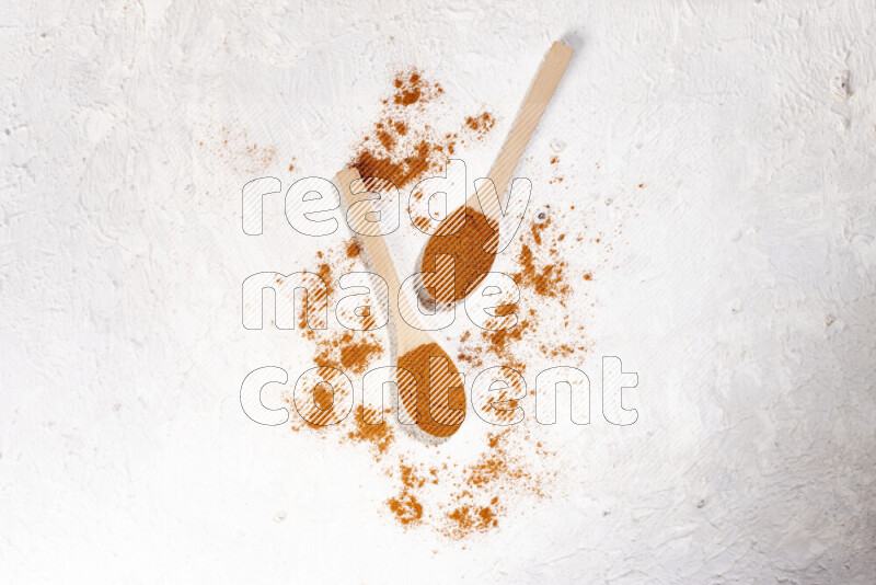 Two wooden spoons full of ground paprika powder on white background