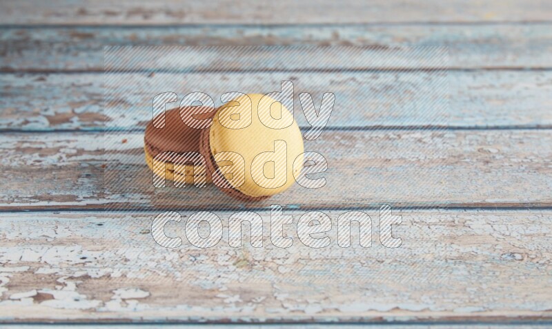 45º Shot of two Yellow and Brown Chai Latte macarons on light blue wooden background