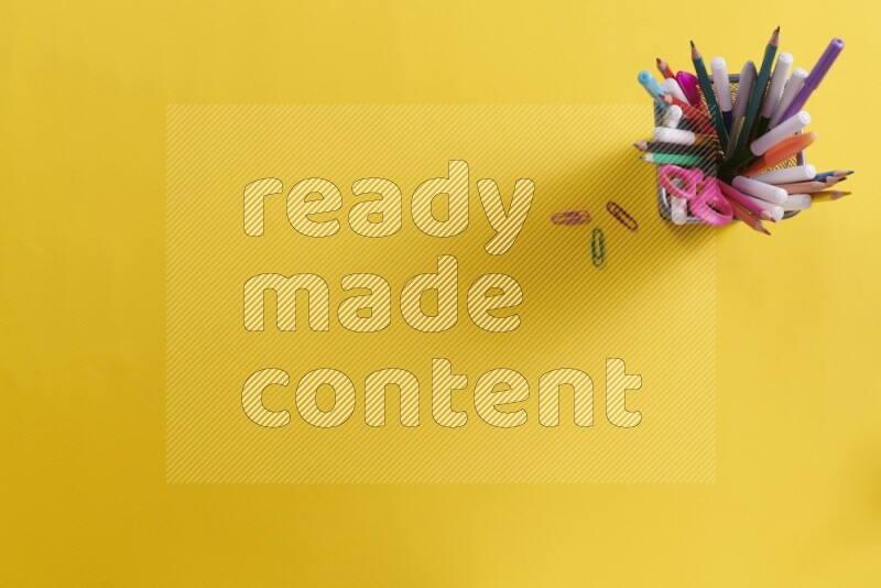 Pens, pencils and school supplies in a metal pen holder on yellow background